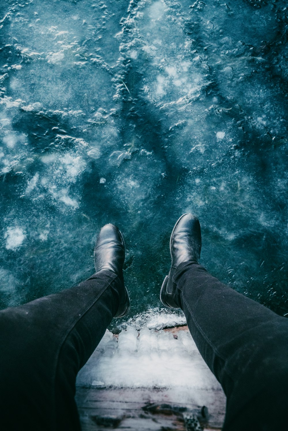 personne en pantalon noir et chaussures en cuir noir debout sur l’eau