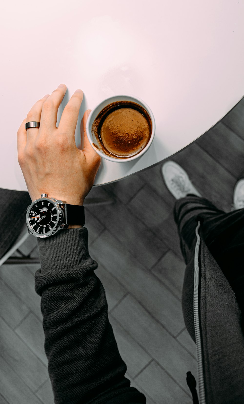 person in black leather strap round analog watch holding white ceramic mug with brown liquid