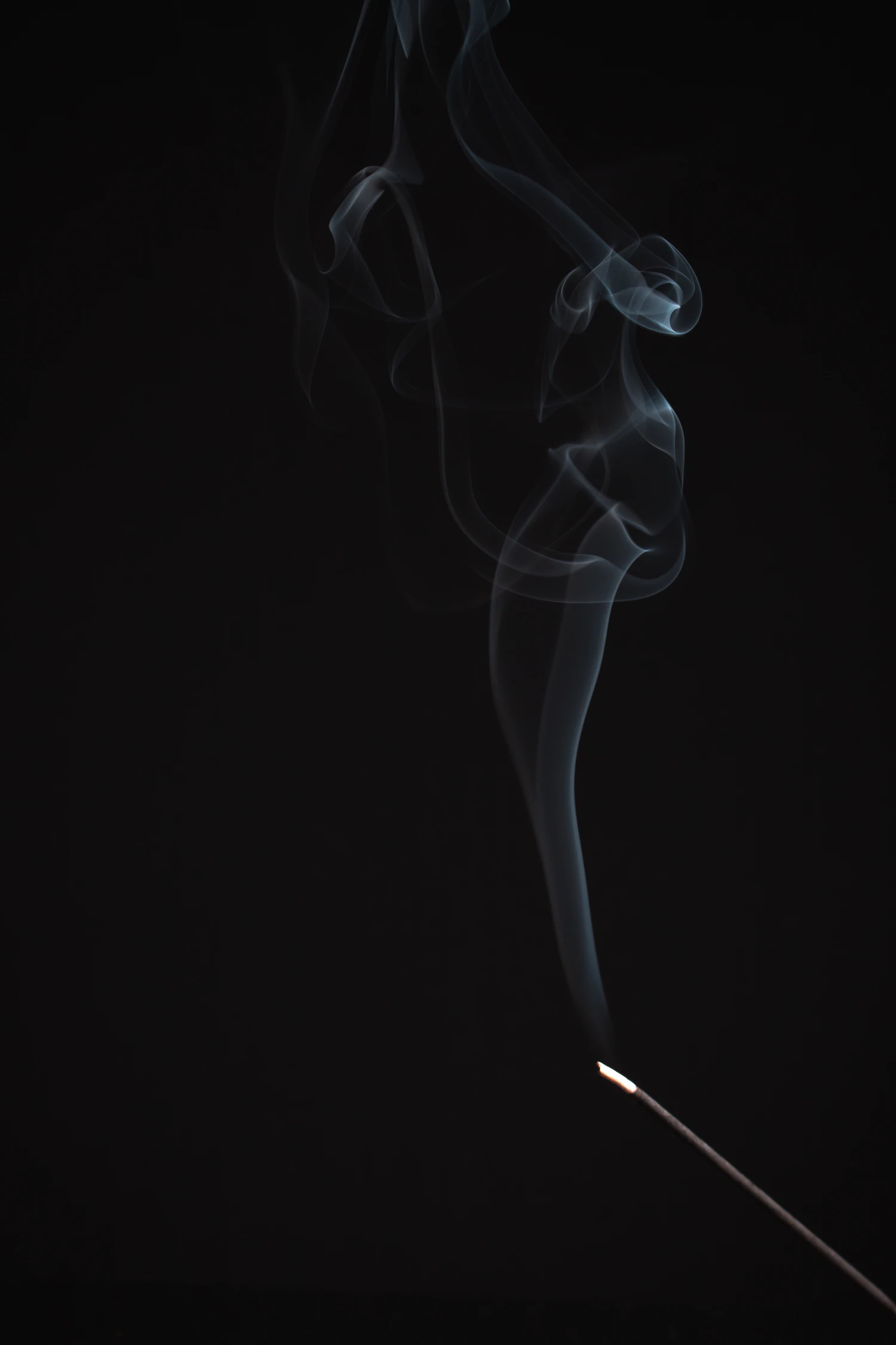 A thread of smoke rising from a burning resin stick in the dark