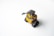 A small, toy-like yellow robot with large binocular-style eyes and track-like wheels is positioned on a smooth white surface. Its mechanical arm is slightly raised, and the design appears both endearing and functional.