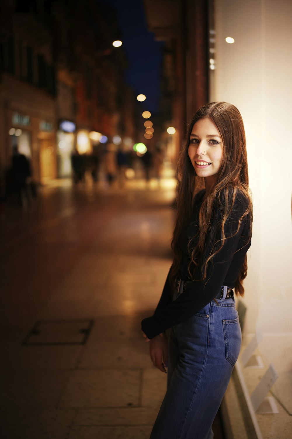 woman in black long sleeve shirt and blue denim jeans standing on sidewalk during daytime