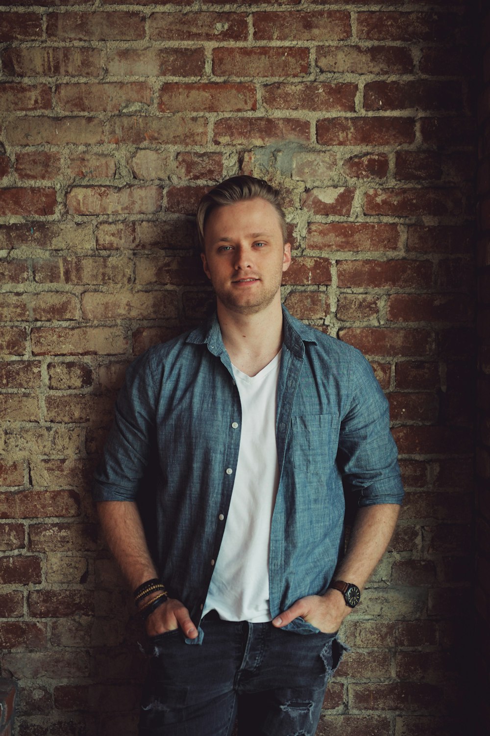 man in blue button up shirt standing beside brown brick wall