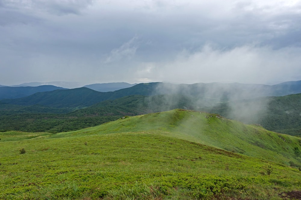 green grass field and mountain under white clouds