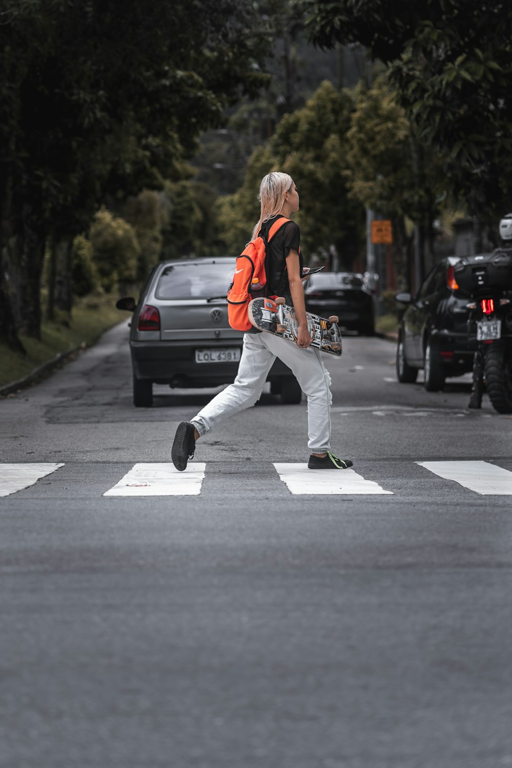 man in orange t-shirt and white pants riding skateboard on gray asphalt road during daytime