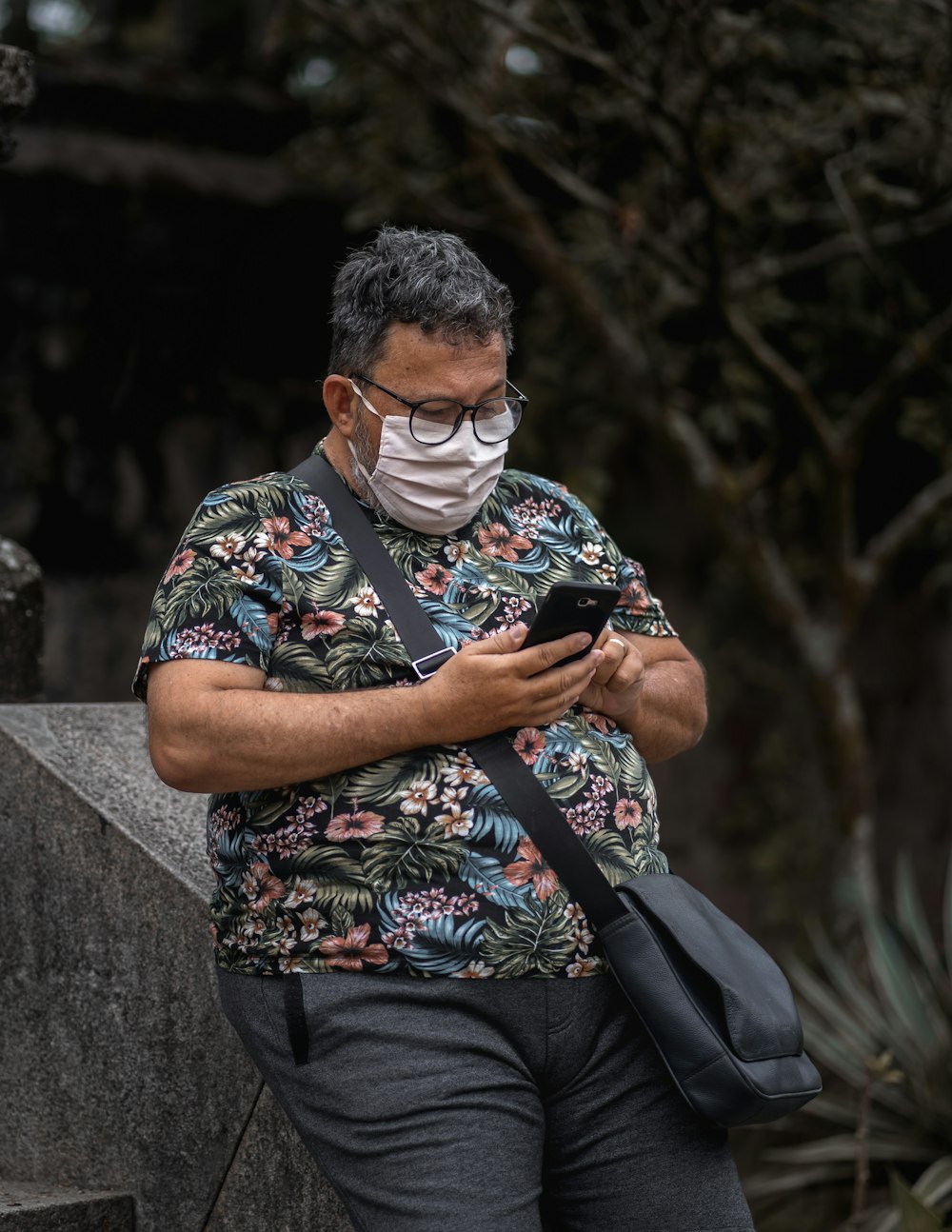 man in white green and floral shirt sitting on gray concrete wall during daytime