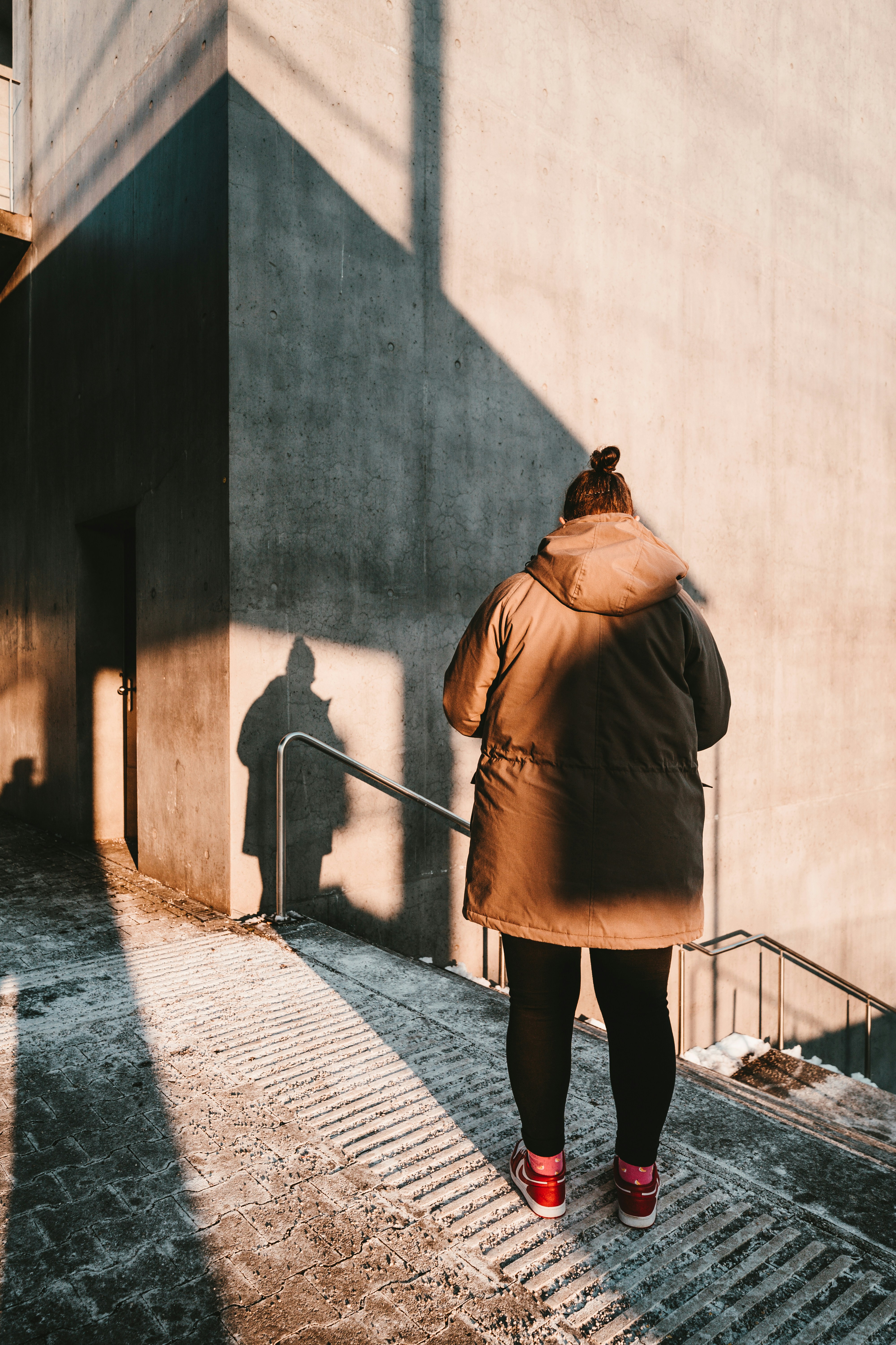 woman in brown coat standing on sidewalk during daytime