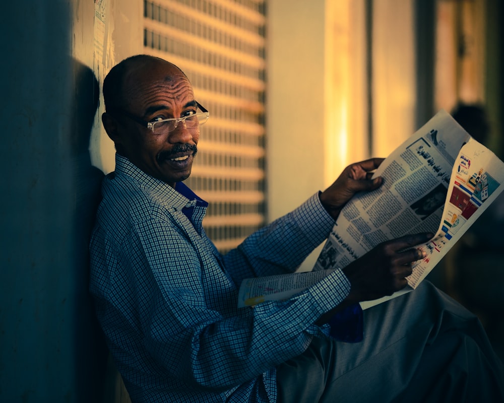 man in blue and white checkered dress shirt reading newspaper