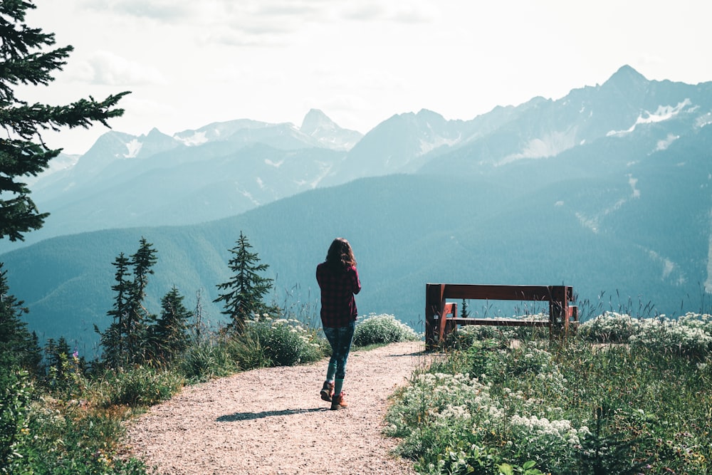 person in black jacket standing on brown dirt road near green trees and mountains during daytime