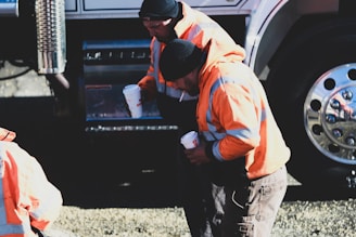 man in orange shirt and black pants standing beside black car during daytime