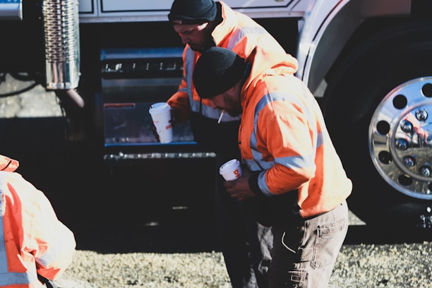 man in orange shirt and black pants standing beside black car during daytime