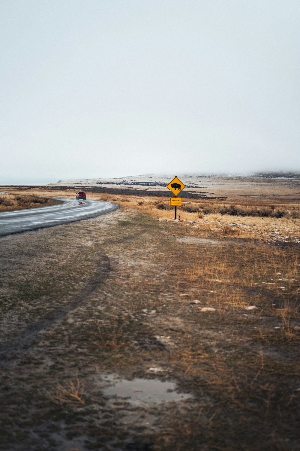 yellow and black road sign on brown field under gray sky