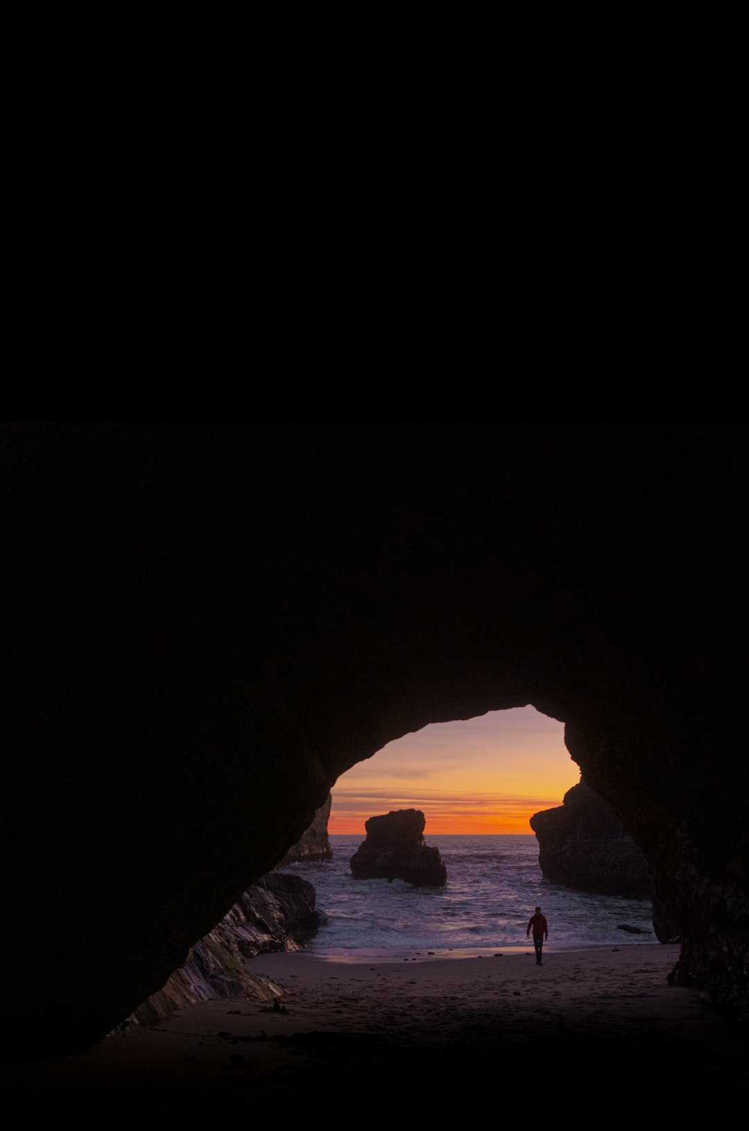 silhouette of person standing on rock formation near body of water during daytime