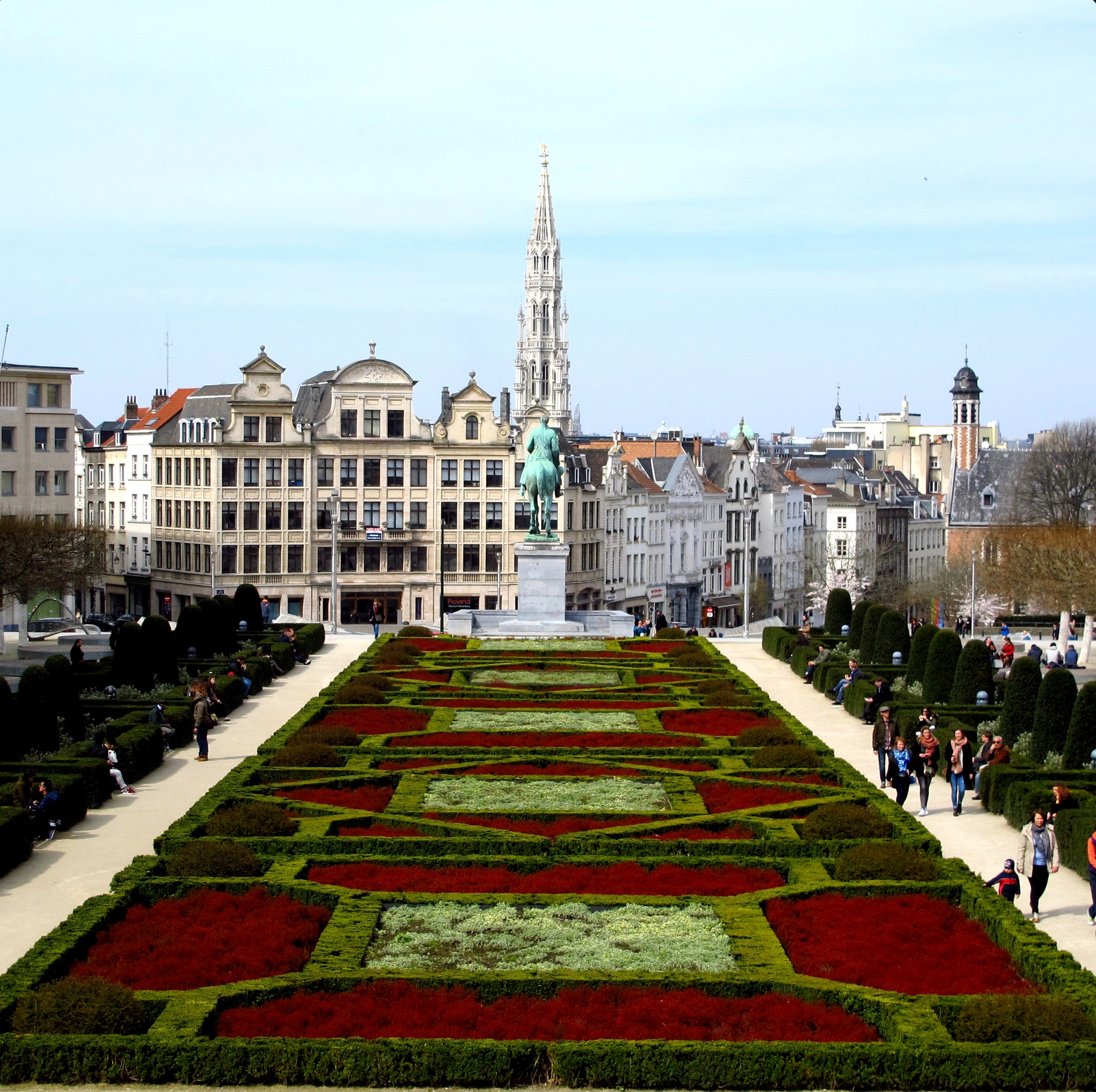 The Mont des Arts garden in Brussels, with clipped hedges, red flower beds and the Town Hall spire in the distance.