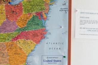 A detailed map of the eastern United States with colorful pushpins marking various locations on the map. States like North Carolina, Virginia, and South Carolina are clearly visible, along with the labels of other states in different colors. To the right of the map is a small informational notice explaining how to leave a mark using the pins. The notice gives instructions and includes a welcoming message.