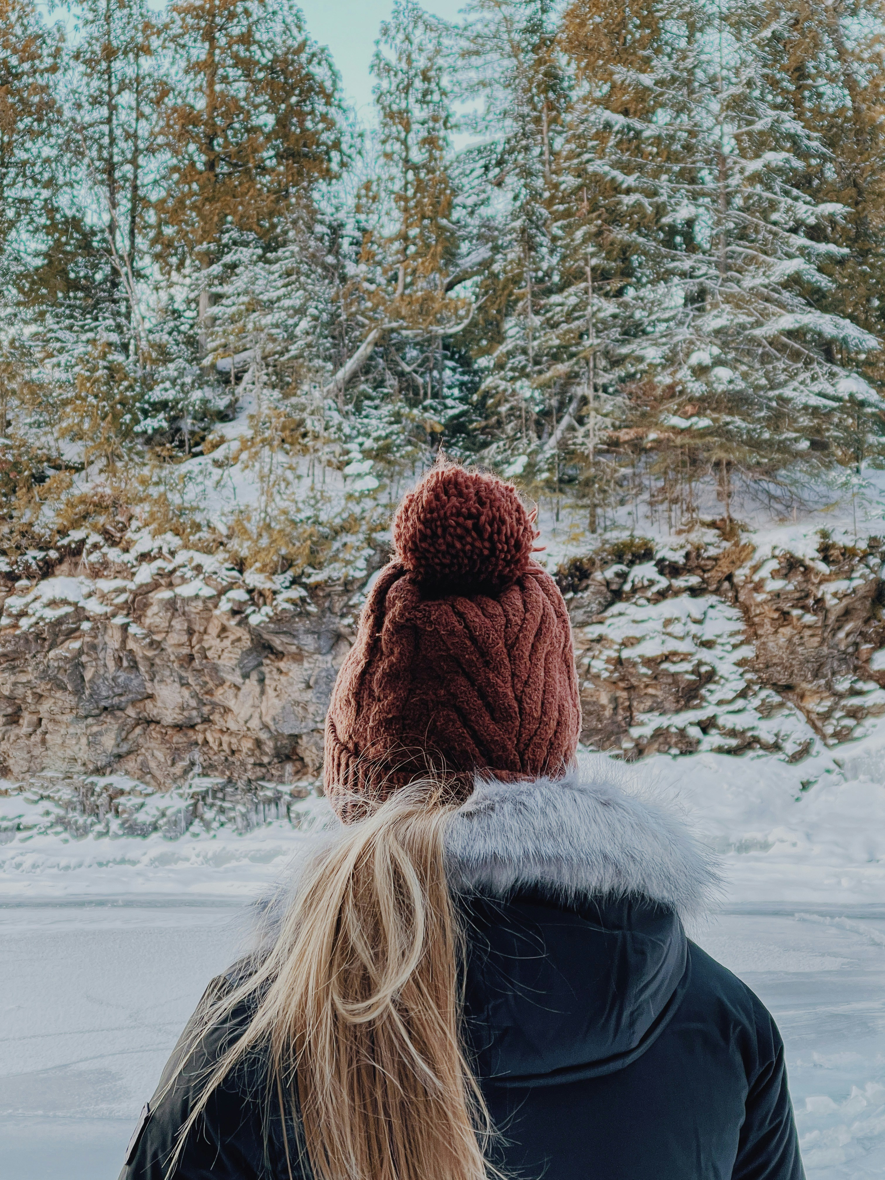 woman in black jacket and brown knit cap standing on snow covered ground during daytime
