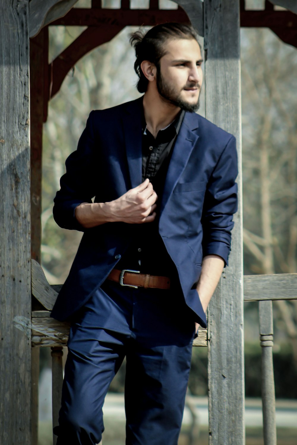 a man in a suit leaning against a wooden structure