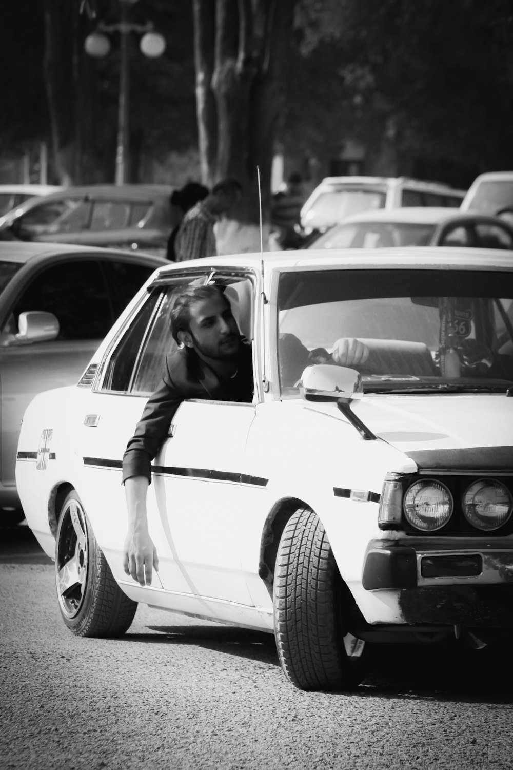 a black and white photo of a man leaning out of a car window