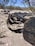 A worn and damaged tire lies on a dry, rocky landscape surrounded by sparse desert vegetation. The tire appears to be shredded and discarded amidst the arid terrain with a clear blue sky visible in the background.