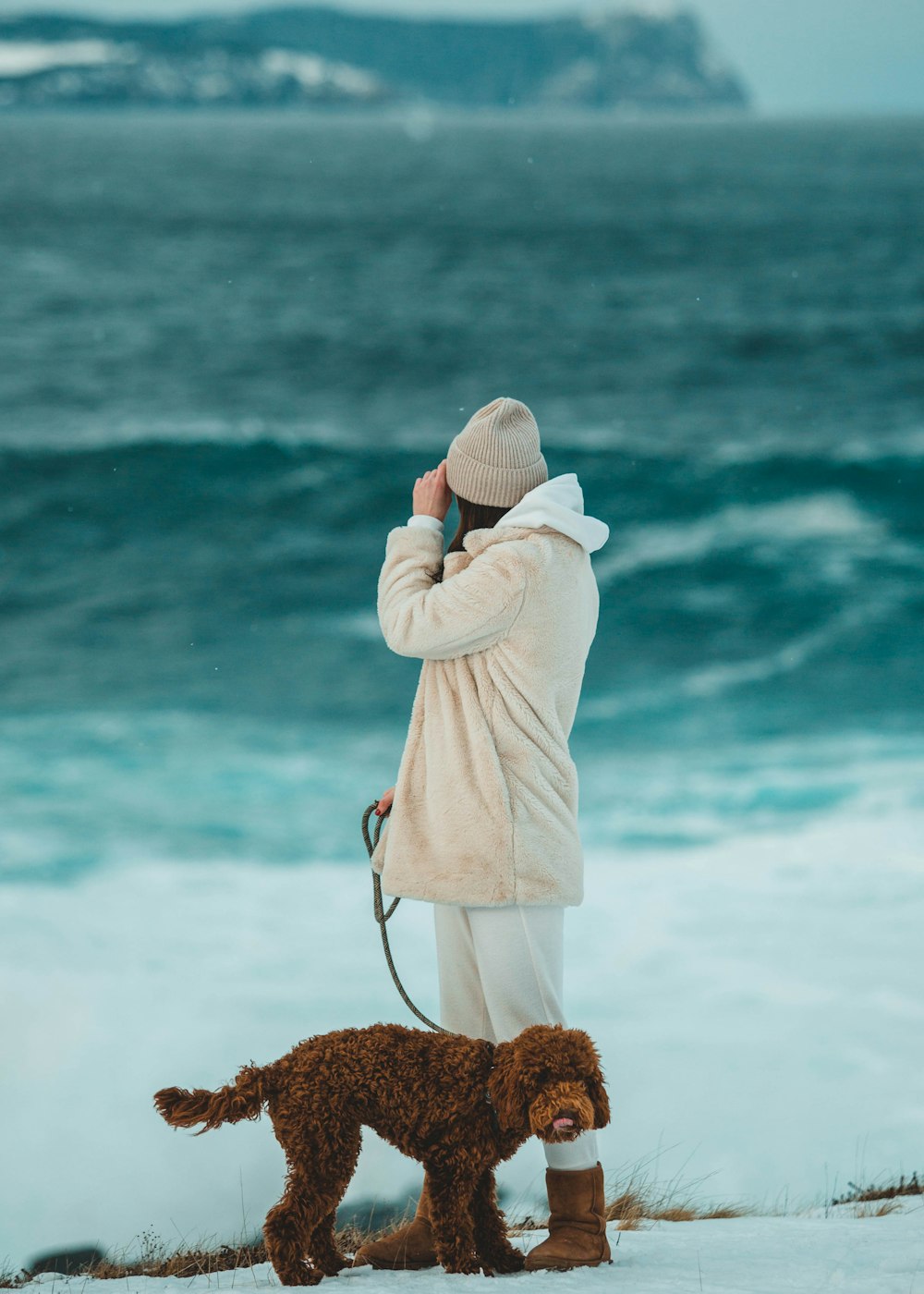 Mujer con sudadera con capucha blanca y gorra de punto blanca de pie en la orilla del mar durante el día