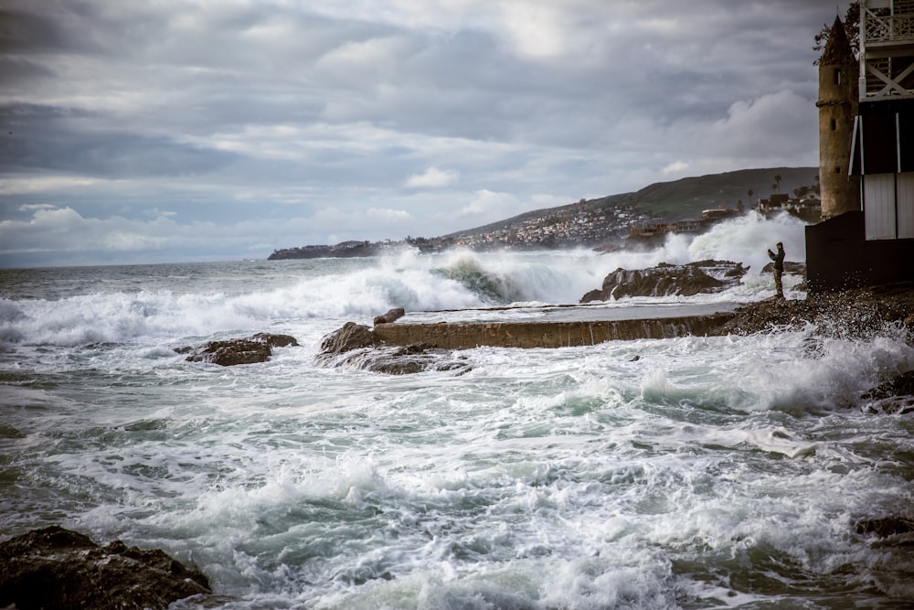 ocean waves crashing on brown rock formation under white clouds during daytime