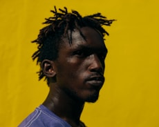 a man with dreadlocks standing in front of a yellow wall