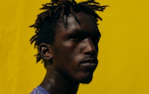 a man with dreadlocks standing in front of a yellow wall