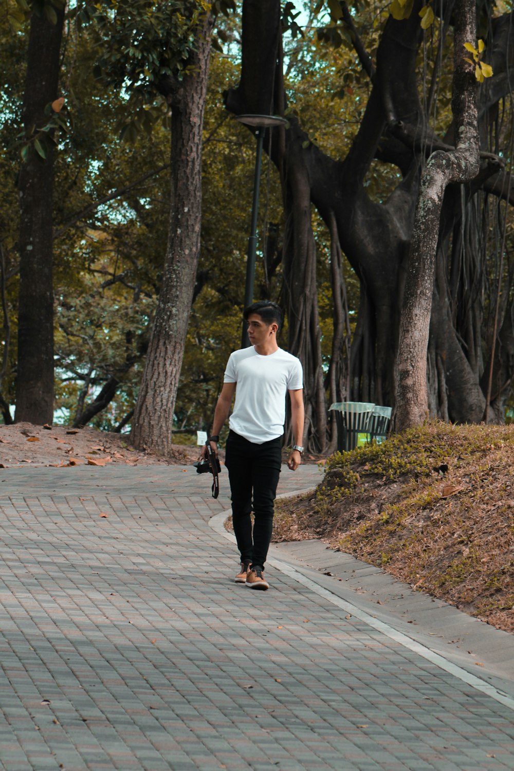 man in white t-shirt and black pants walking on sidewalk during daytime