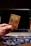 A hand is holding a Pokémon trading card featuring a character named Glumanda. The card is in the foreground with a laptop in the background. Several Pokémon card backs are scattered on a wooden surface.