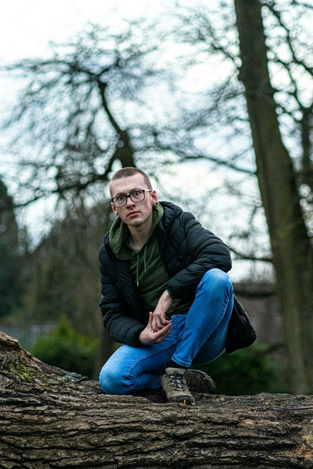 man in black jacket and blue denim jeans sitting on tree log