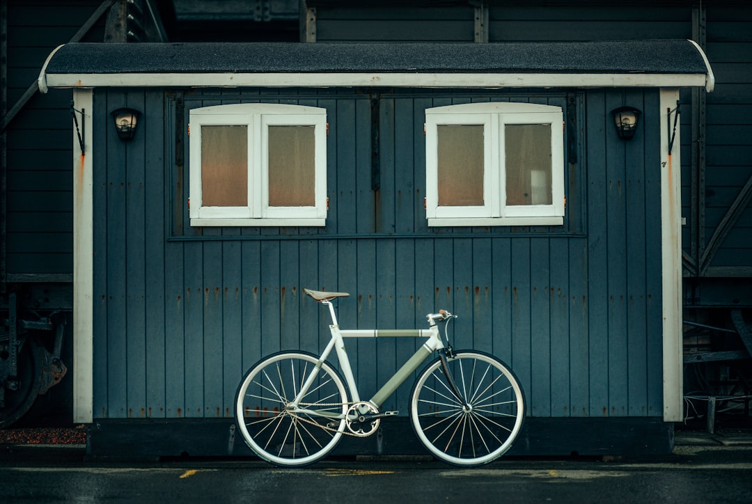 white and blue city bike parked beside gray wooden house