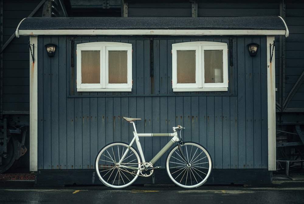 white and blue city bike parked beside gray wooden house