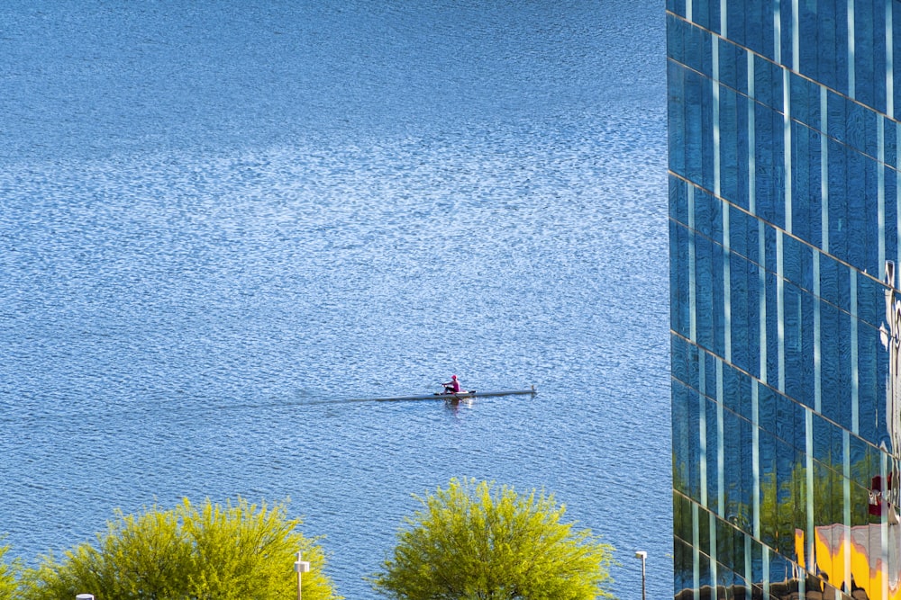 person in red shirt and black pants standing on blue concrete building near body of water