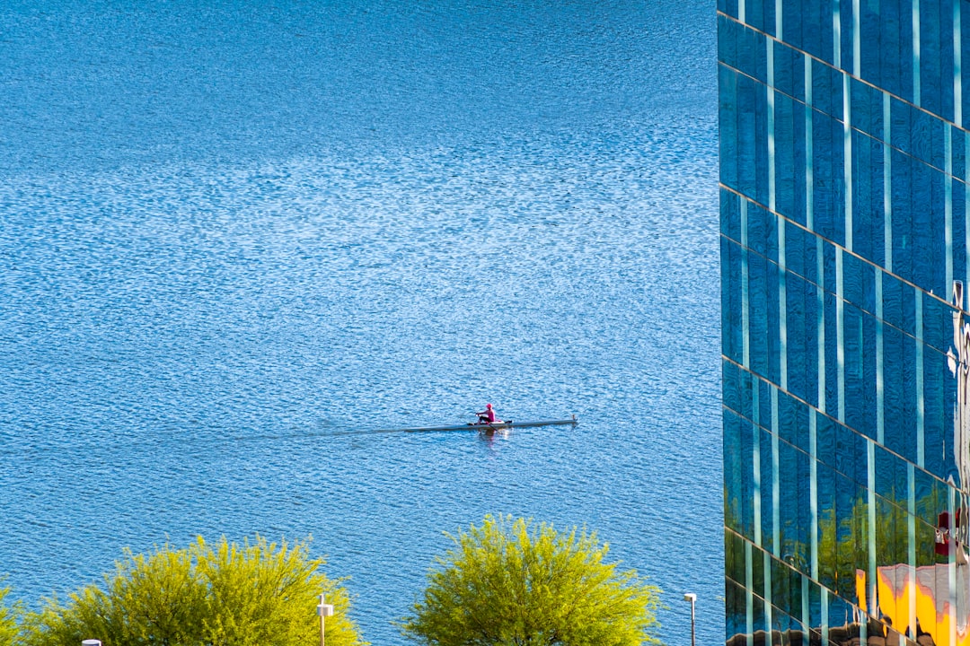 person in red shirt and black pants standing on blue concrete building near body of water