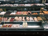 A well-lit pastry display case featuring an array of baked goods. The assortment includes croissants, cannoli, tarts, and various pastries decorated with powdered sugar, fruit, and chocolate. The shelves are organized with different kinds of sweets, creating an inviting and appetizing presentation.