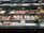 A well-lit pastry display case featuring an array of baked goods. The assortment includes croissants, cannoli, tarts, and various pastries decorated with powdered sugar, fruit, and chocolate. The shelves are organized with different kinds of sweets, creating an inviting and appetizing presentation.
