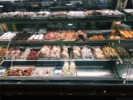 A well-lit pastry display case featuring an array of baked goods. The assortment includes croissants, cannoli, tarts, and various pastries decorated with powdered sugar, fruit, and chocolate. The shelves are organized with different kinds of sweets, creating an inviting and appetizing presentation.