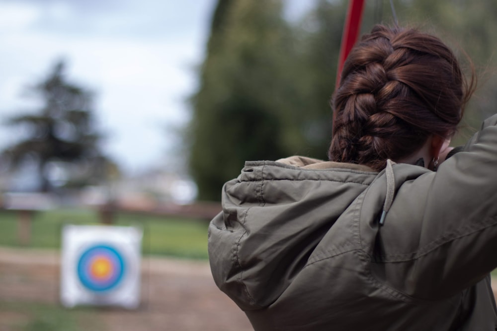 personne en veste brune debout près d’un champ d’herbe verte pendant la journée