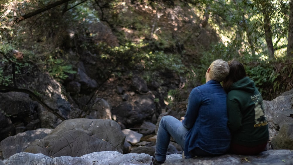 woman in blue long sleeve shirt sitting on gray rock during daytime