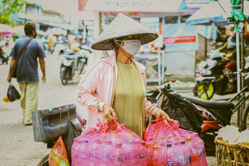 woman in pink long sleeve shirt and brown sun hat carrying pink plastic bags