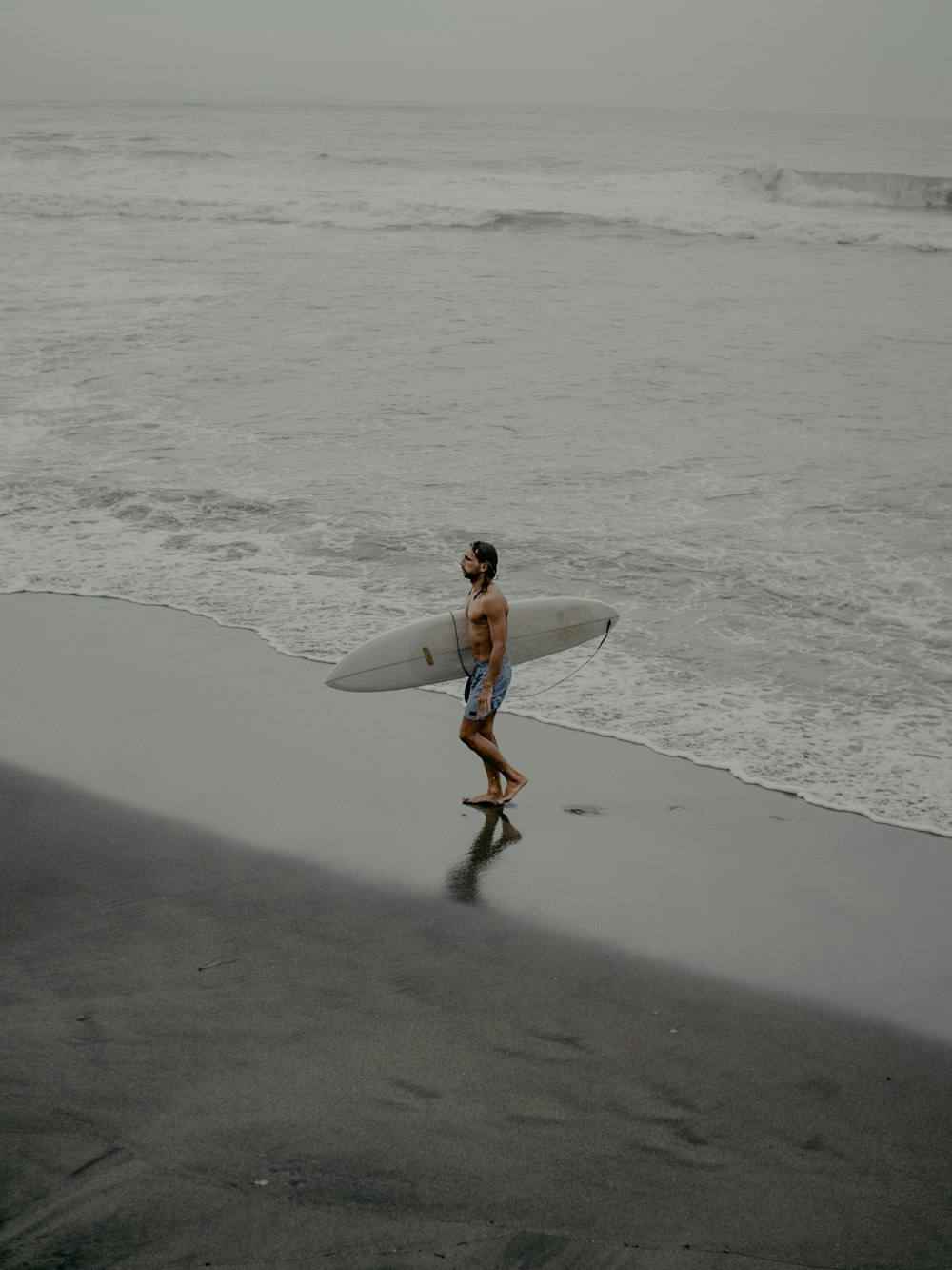 uomo in camicia bianca che tiene la tavola da surf bianca che cammina sulla spiaggia durante il giorno