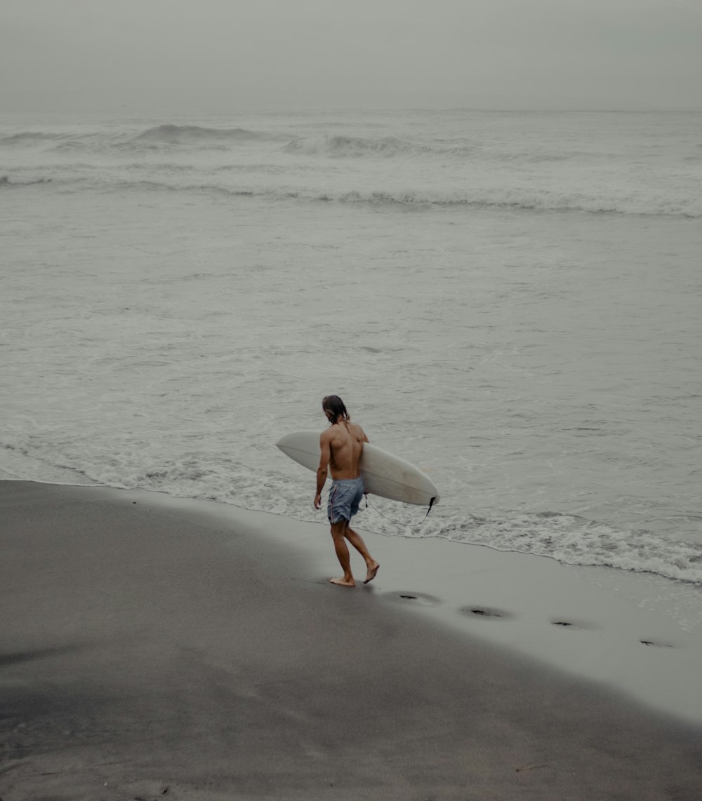 woman in white tank top and blue denim shorts walking on beach during daytime