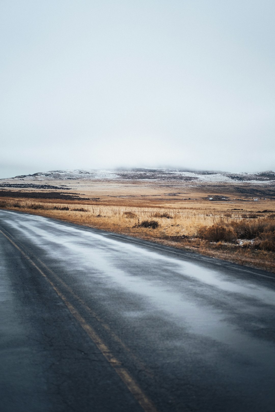 gray asphalt road between brown grass field under white sky during daytime