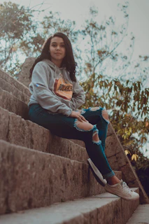 A laid-back scene of a man in a hoodie and sneakers, sitting on urban steps with a relaxed smile.