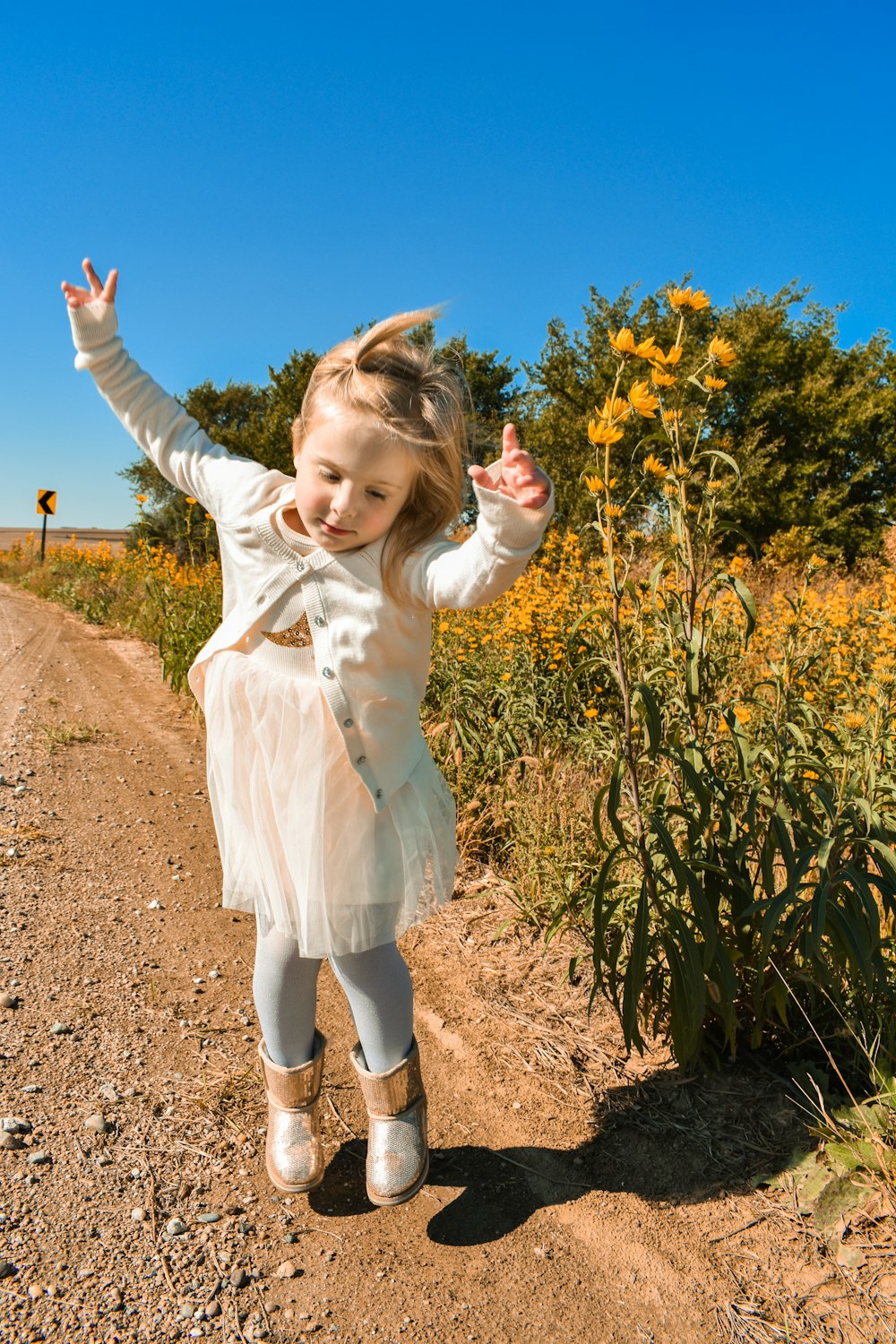 girl in white dress shirt and blue denim jeans standing on brown soil during daytime