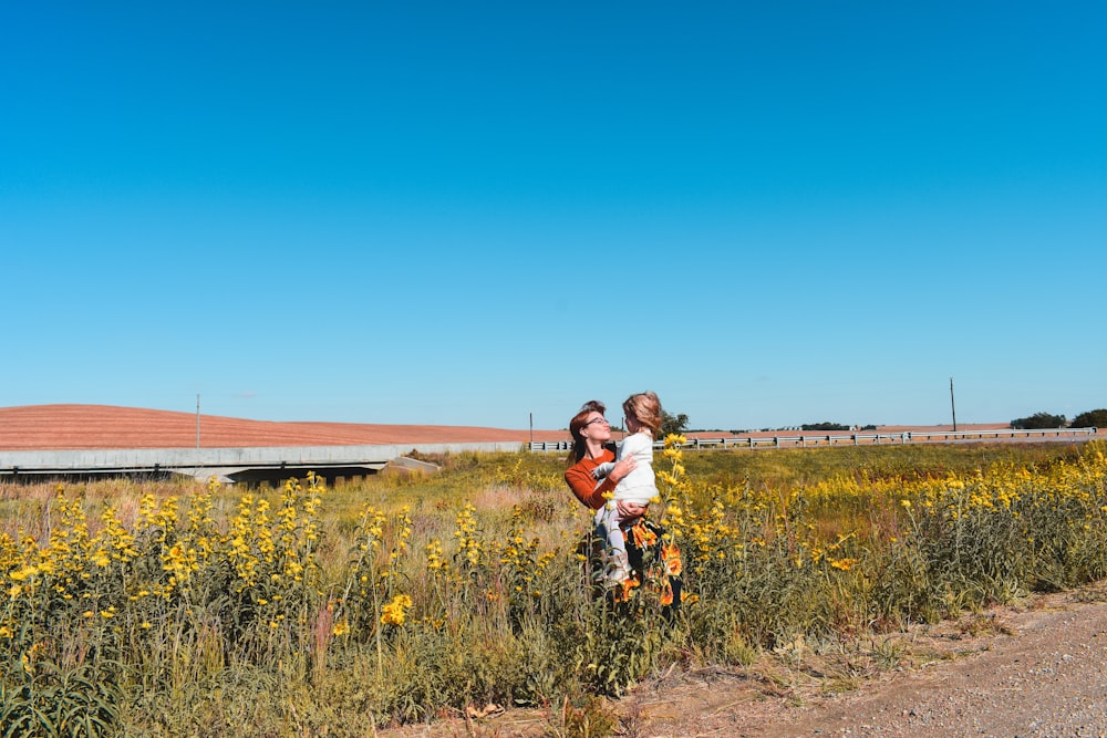 woman in white long sleeve shirt carrying child in white long sleeve shirt on green grass