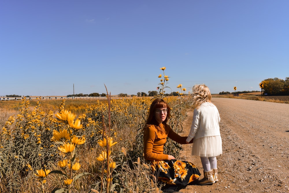 woman in brown long sleeve shirt sitting on yellow flower field during daytime