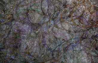 A complex and abstract pattern featuring numerous overlapping elliptical and circular lines intertwined at various angles, creating a sense of depth. The lines appear dotted and vary in color, giving a dynamic and chaotic feel to the composition, which is set against a textured background.
