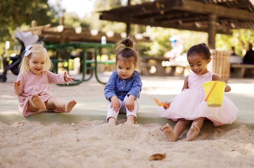 Group of toddlers exploring sensory play with sand and natural materials outdoors.