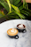 Two cups of coffee with latte art, one with a heart pattern and the other with a leaf design, placed on a white marble table. Green tropical plants are visible in the background, creating a serene and natural setting.