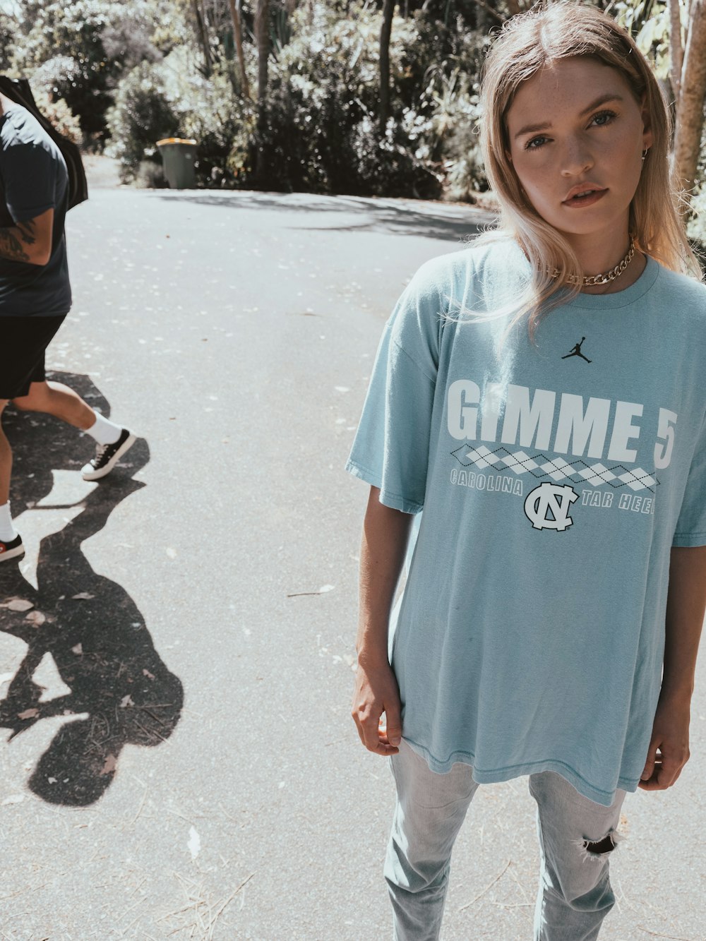 낮 동안 회색 모래 위에 서 있는 파란색 크루넥 티셔츠를 입은 소녀